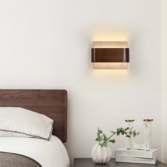 Sconce lit above a bed beside a nightstand with two small glass vases