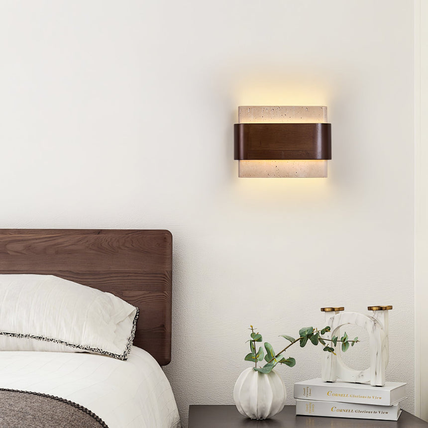 Sconce lit above a bed beside a nightstand with two small glass vases