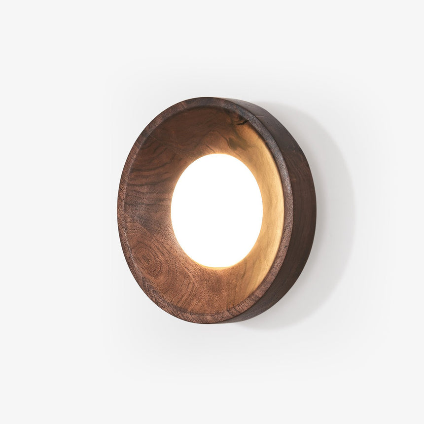 Wall sconce above a bed, a straight sided wood drum with a lit white disc