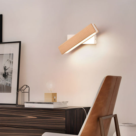 Sconce lit above a dark console with framed prints and a wood chair below