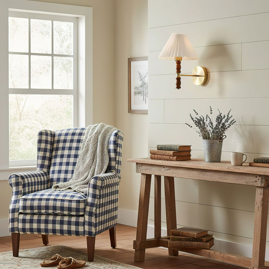 Pleated wall sconce lit above a console table beside a checked armchair
