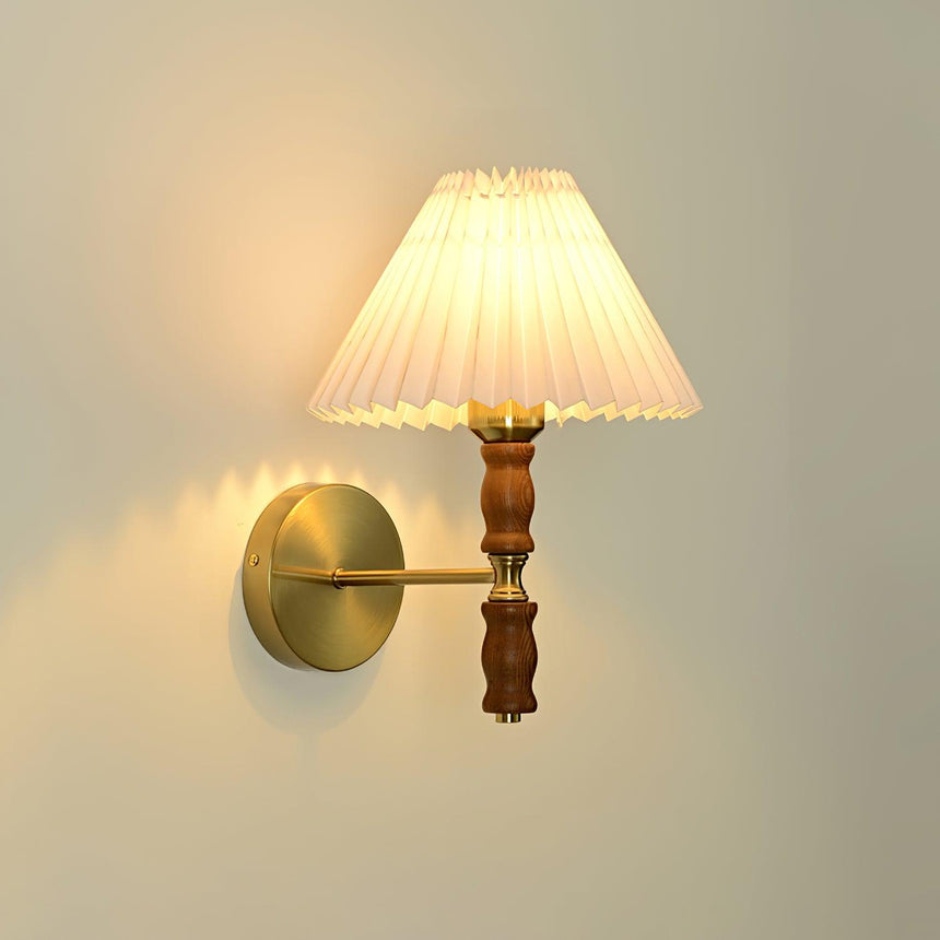 Warm light through a pleated linen shade on a walnut and brass sconce