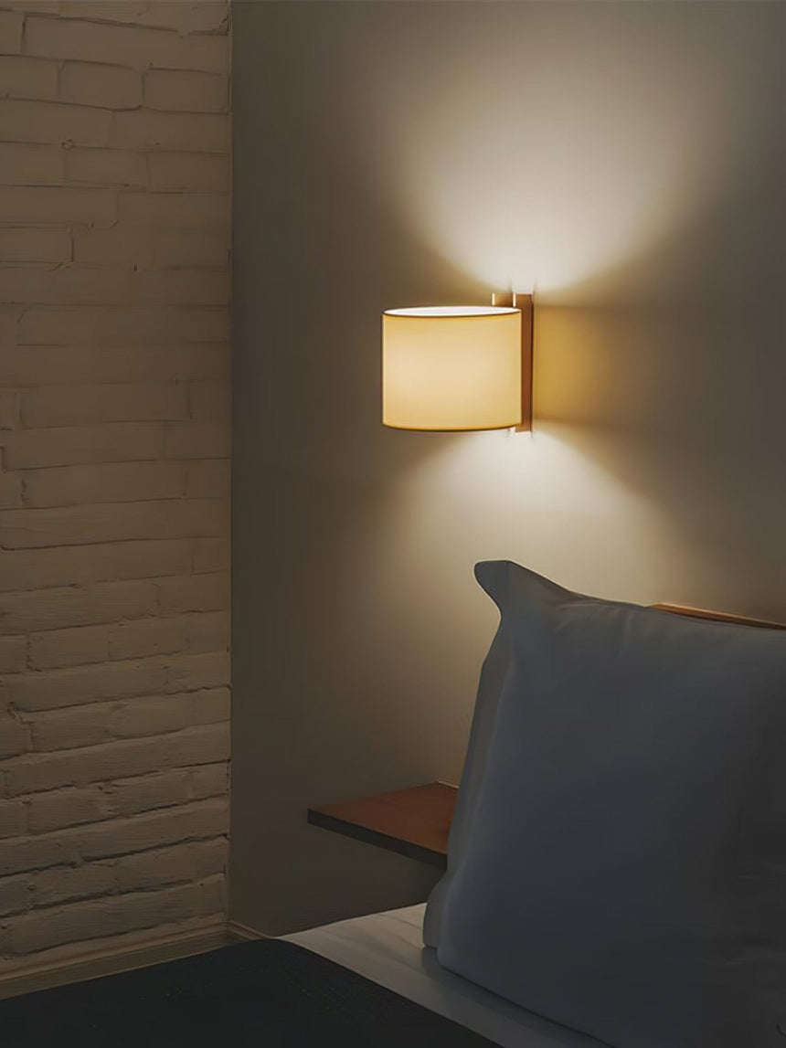 Sconce lit on a brick wall beside a bed with a slate blue cushion