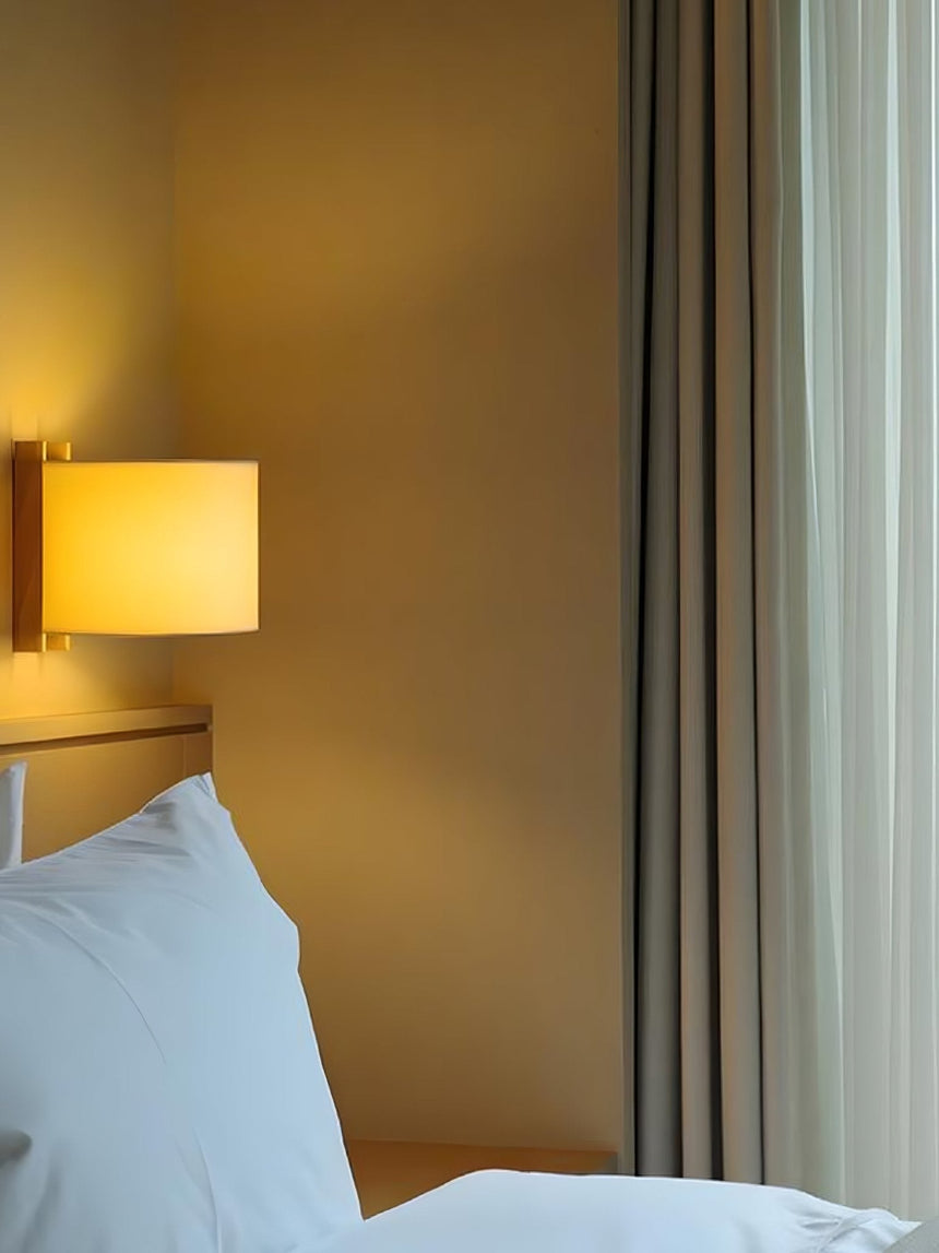 Sconce lit beside a bed with white pillows and a curtain drawn at the side