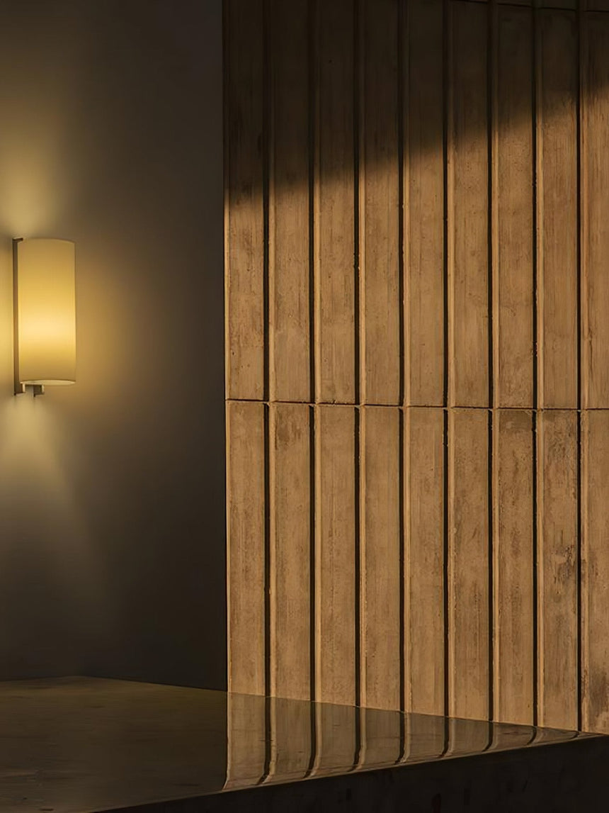 Sconce lit beside a slatted wood wall, the shade glowing warm against it