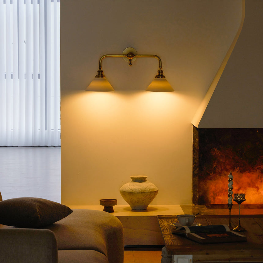 The double sconce lit above a fireplace wall, a low table and a ceramic vase below