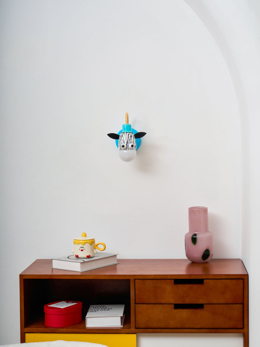 The zebra lamp on a white wall above a wood dresser and a vase