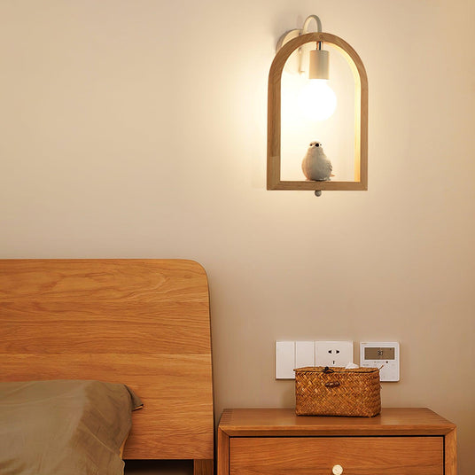 Sconce lit above a wood nightstand holding a basket beside a bed