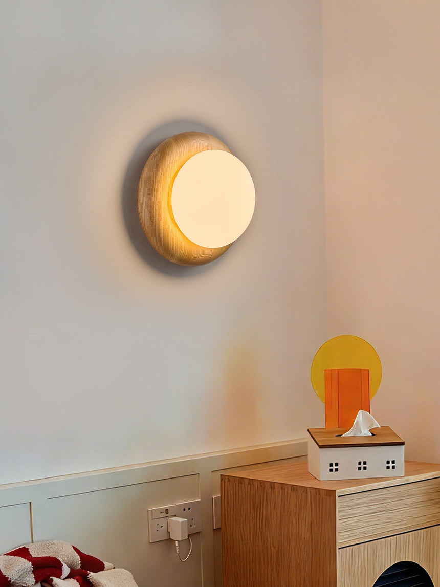 Sconce lit on a pale wall above a wood cabinet holding an amber glass lamp