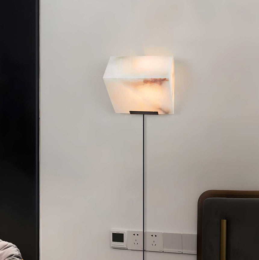 The single block lamp on a wall above an outlet, its cord running to the plug