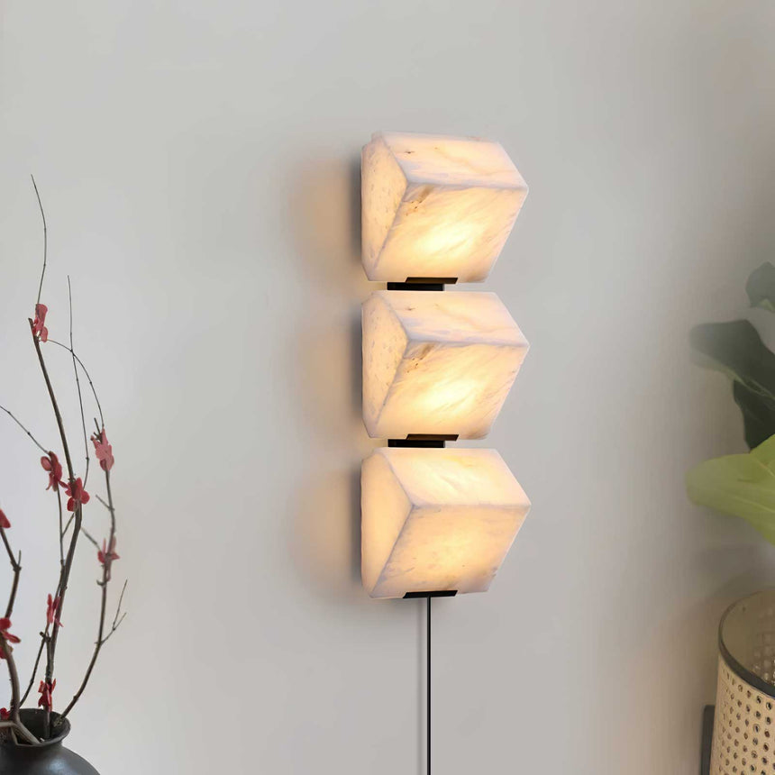 Three lit alabaster blocks on a pale wall beside a branch in a vase