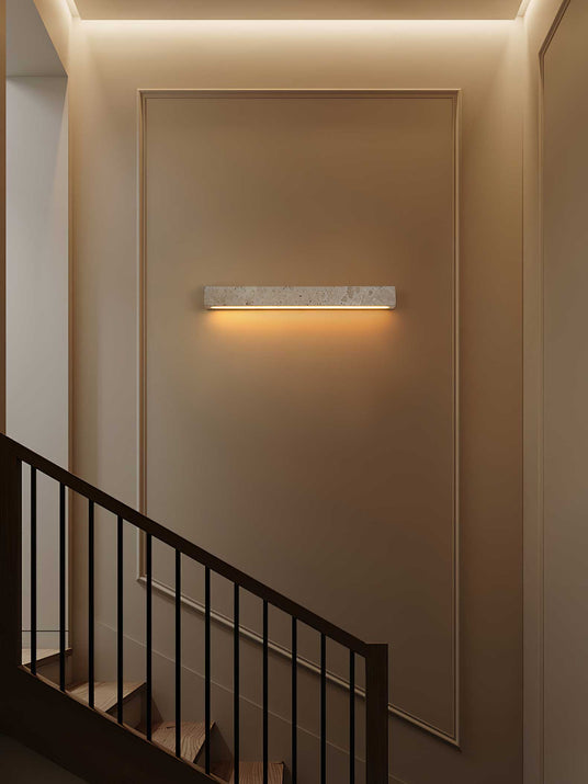 Travertine bar lit on a stairwell wall above a black metal balustrade and steps