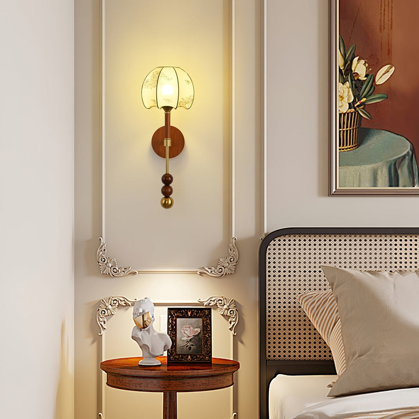Walnut column sconce lit beside a bed above a round side table