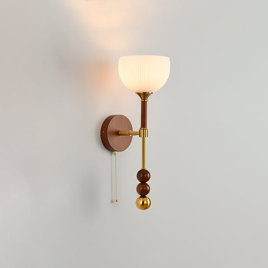 Close view of a lit white bell shade on a walnut and brass wall sconce