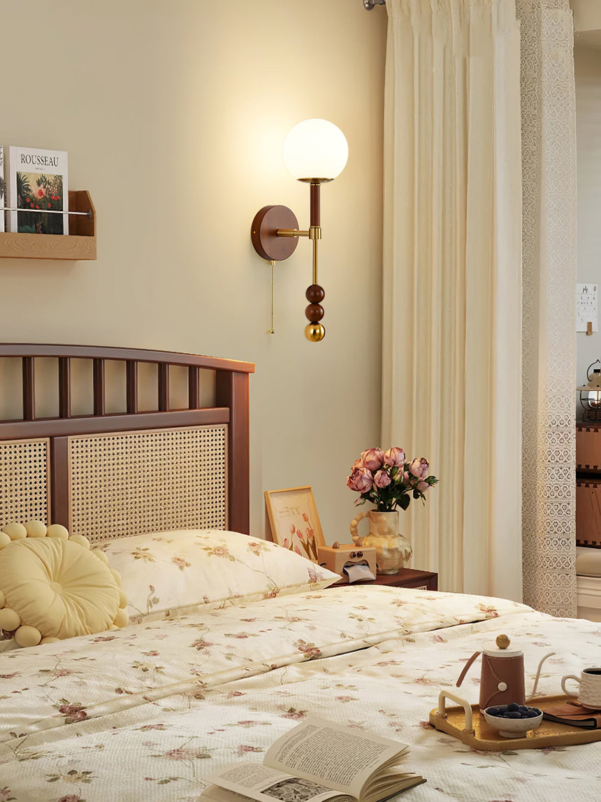 Walnut column sconce lit on a bedroom wall beside a spindle headboard