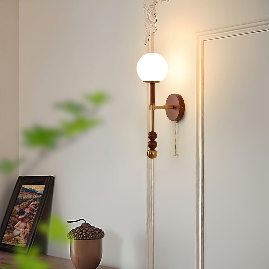 Walnut column sconce lit on a paneled wall above a chest of drawers