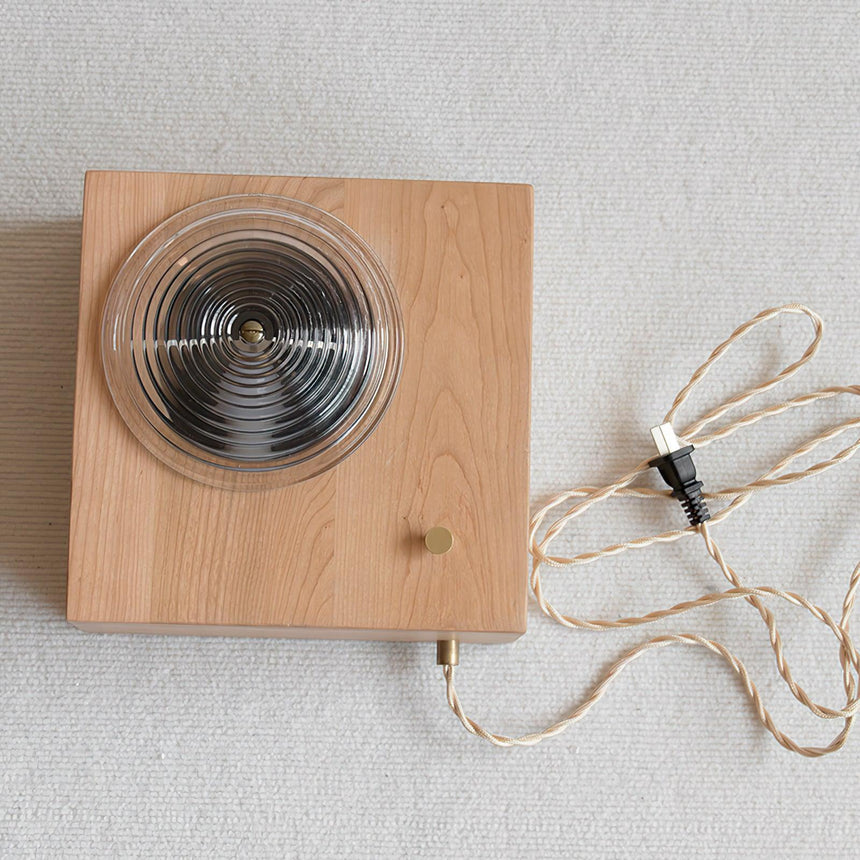 The wood box laid flat showing the ribbed lens and the braided fabric cord