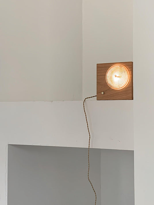Wood box sconce lit high on a wall in a corner, the cord running down