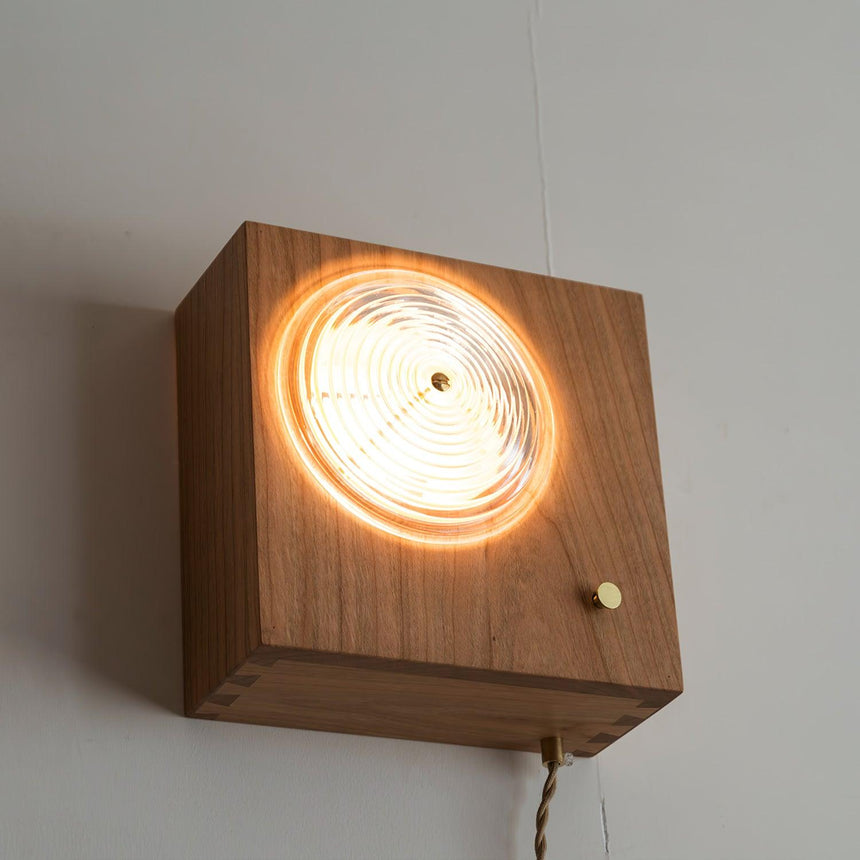 Cherry wood box lit through its ribbed glass lens on a pale wall