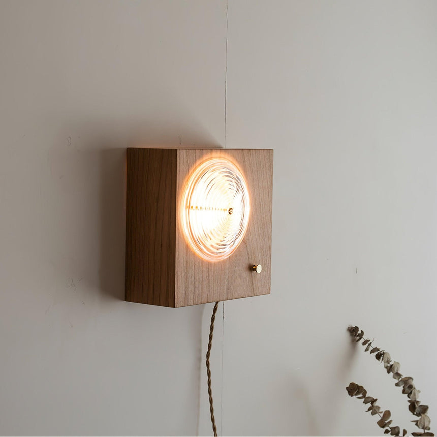 Wood box sconce lit on a white wall with dried stems beside it