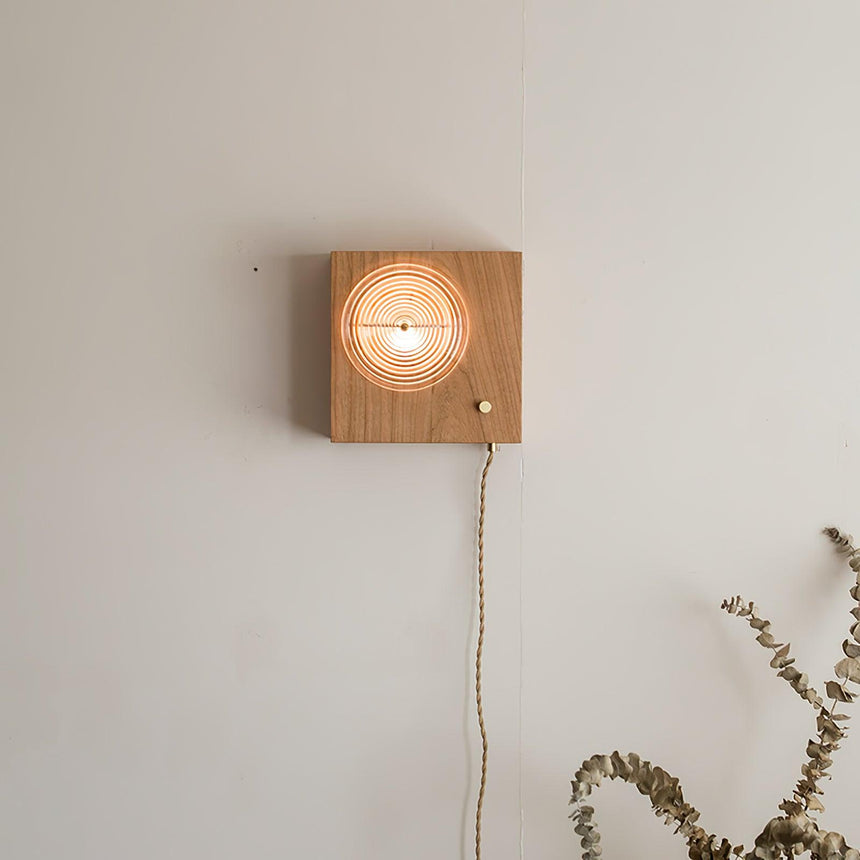 Wood box sconce lit on a plain wall, the cord hanging straight below