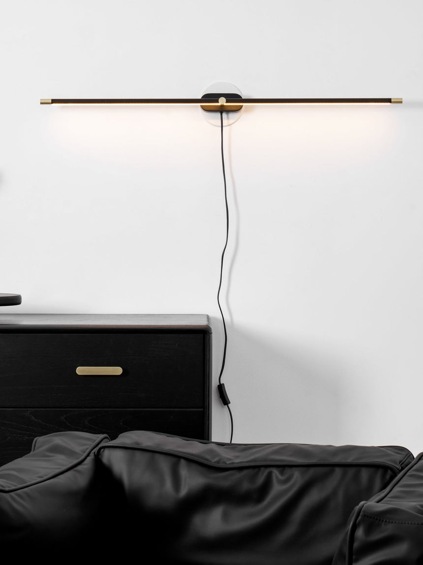 Rod lit above a black drawer unit and a leather chair, the cord loose on the wall