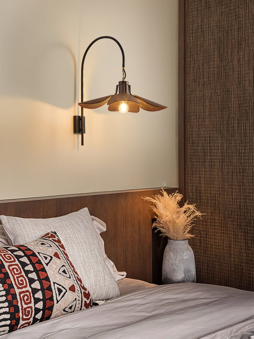 Sconce lit above a bed with a wood headboard and woven cushions