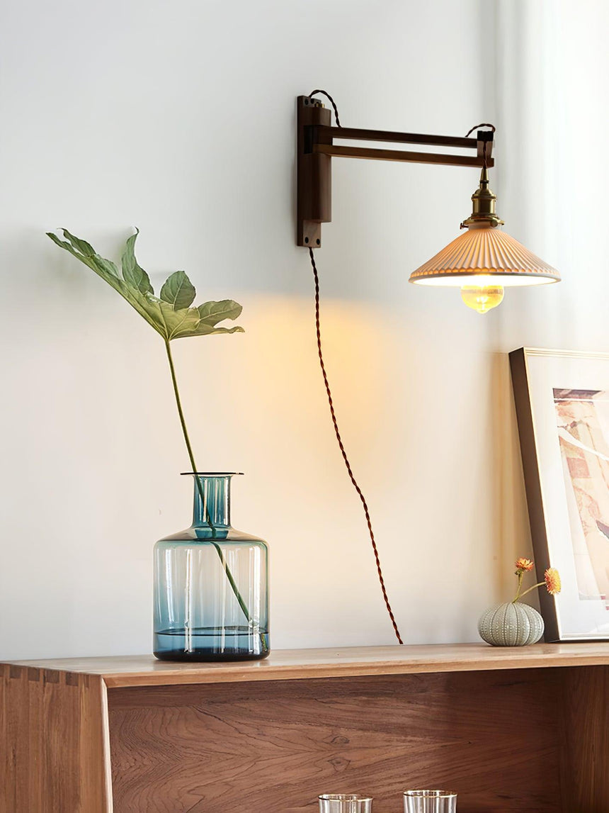 The lamp above a walnut shelf with a blue glass vase and a leafy stem