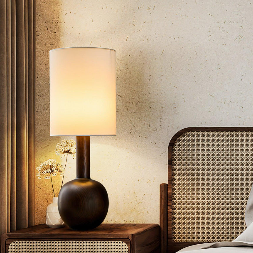 The black version lit on a console beside a cane headboard