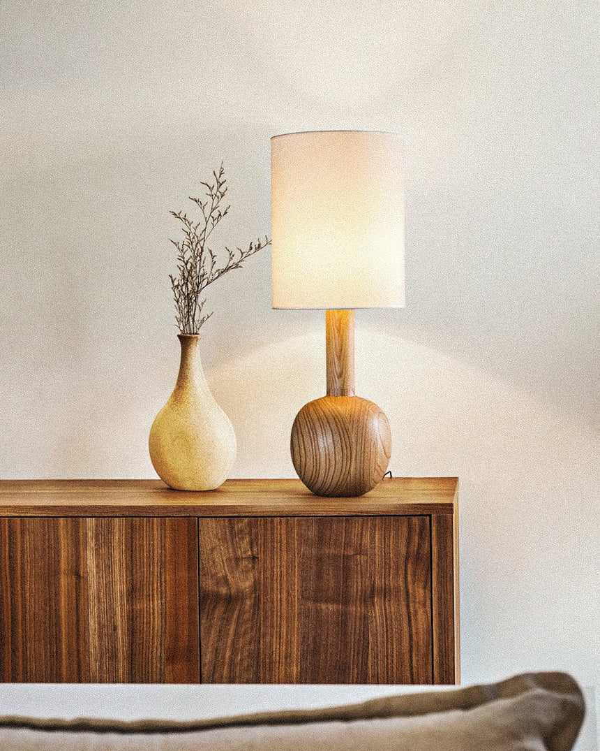 Walnut table lamp lit on a walnut sideboard beside a vase
