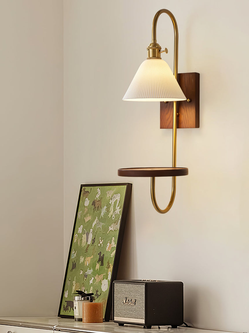 Sconce lit beside a leaning framed print with objects on the shelf