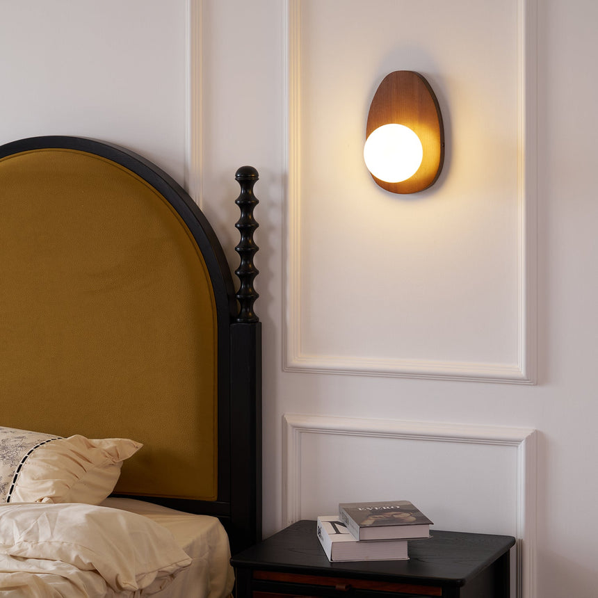 Sconce lit above a bed with a black nightstand holding a stack of books