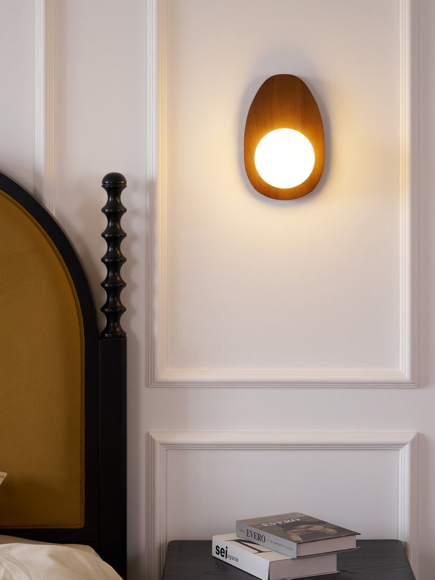 Sconce lit beside a bed above a black nightstand with books and a magazine