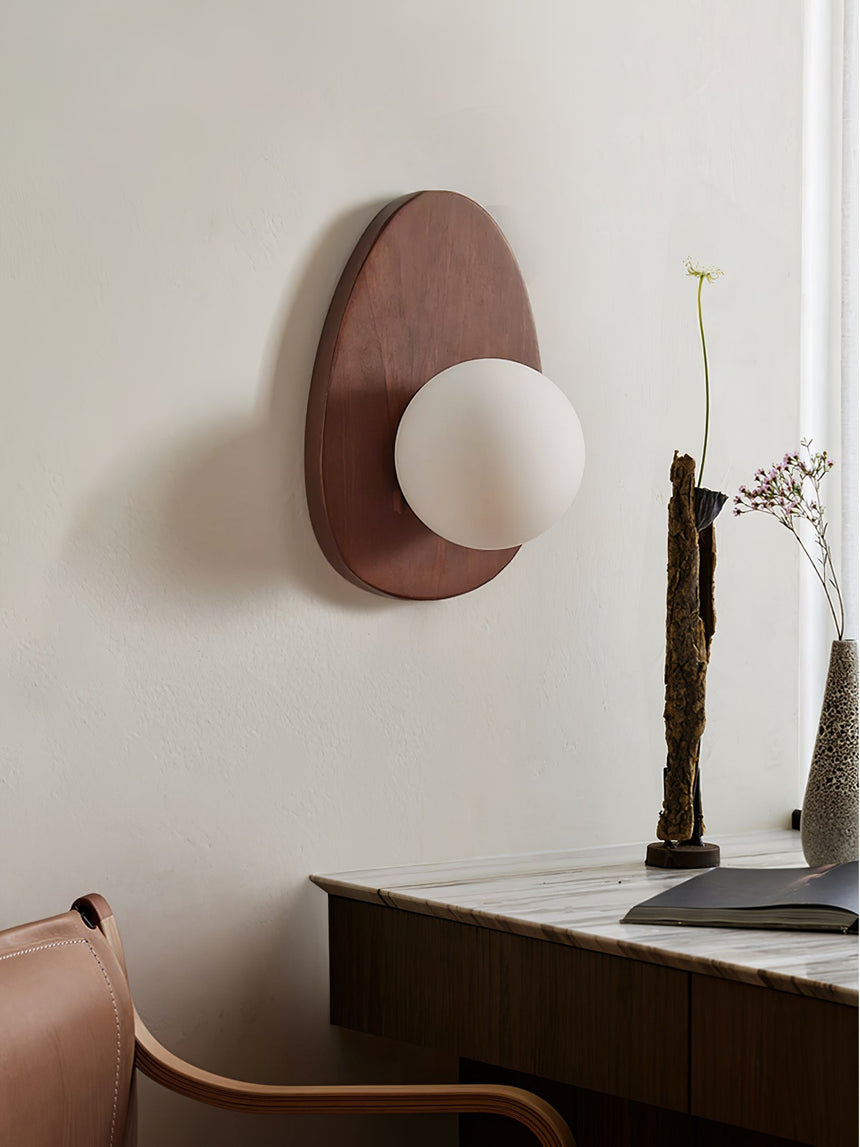 Sconce lit beside a dark console holding a vase of tall dried stems