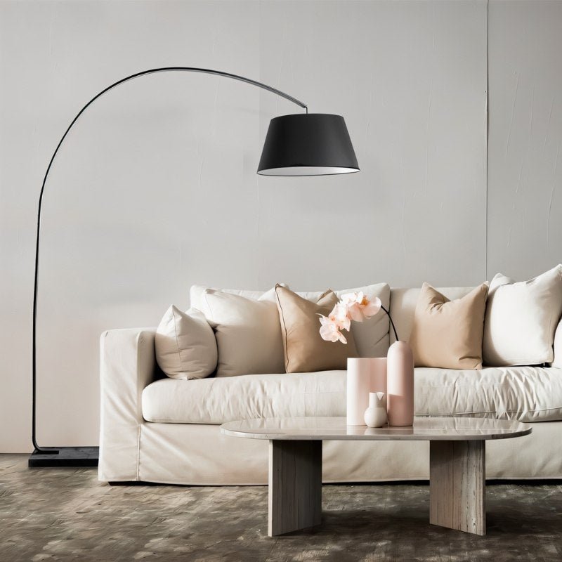 The lamp arching over a white sofa with cushions beside a pale round table