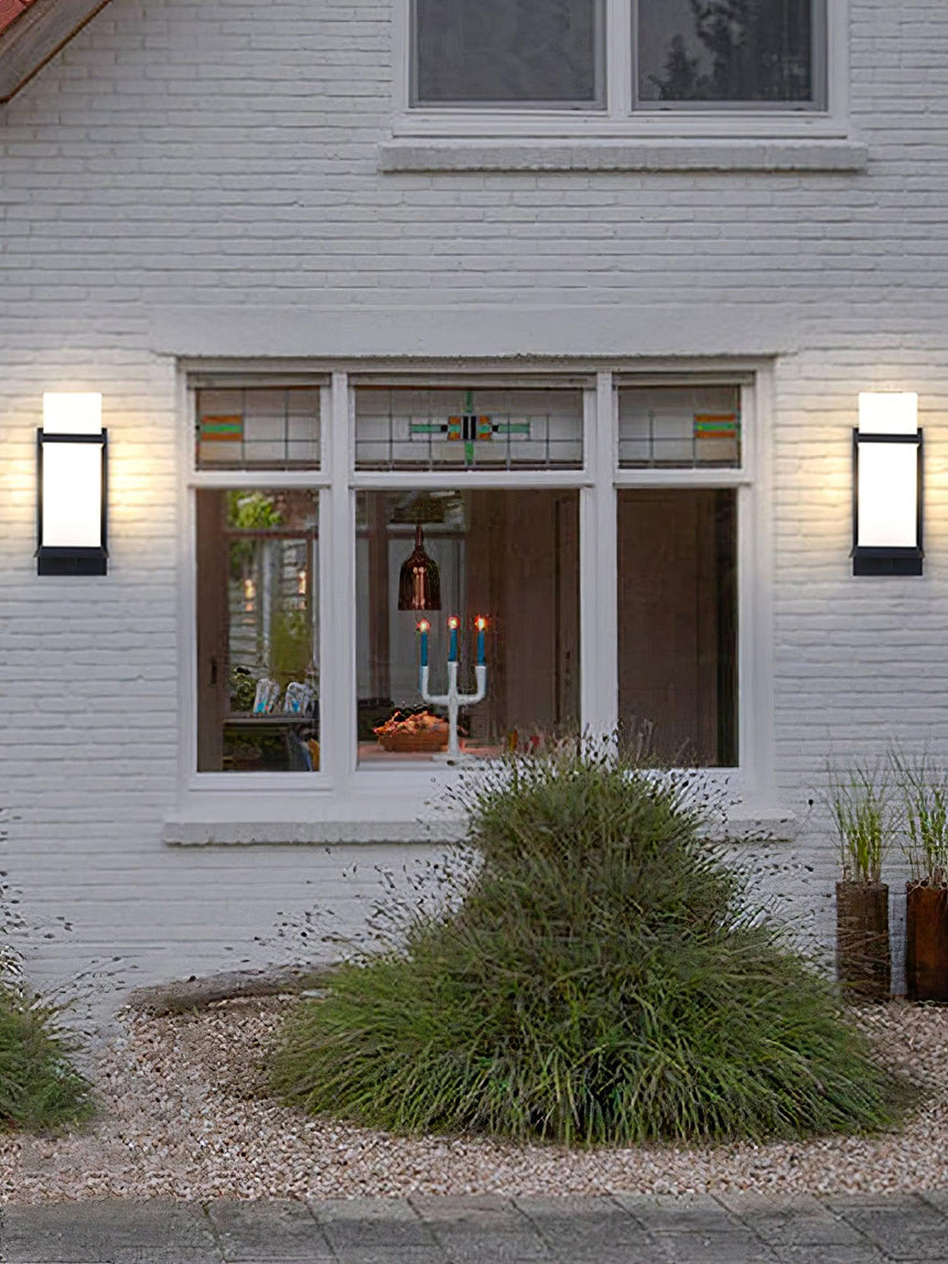Two lights on a white brick house either side of a front window, ornamental grass below