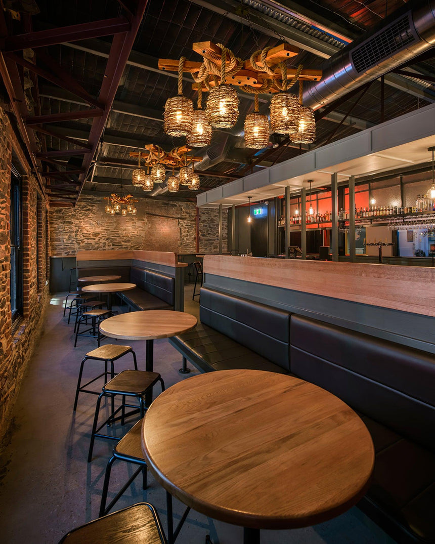 Lit above round wood tables and stools in a bar with brick and dark walls