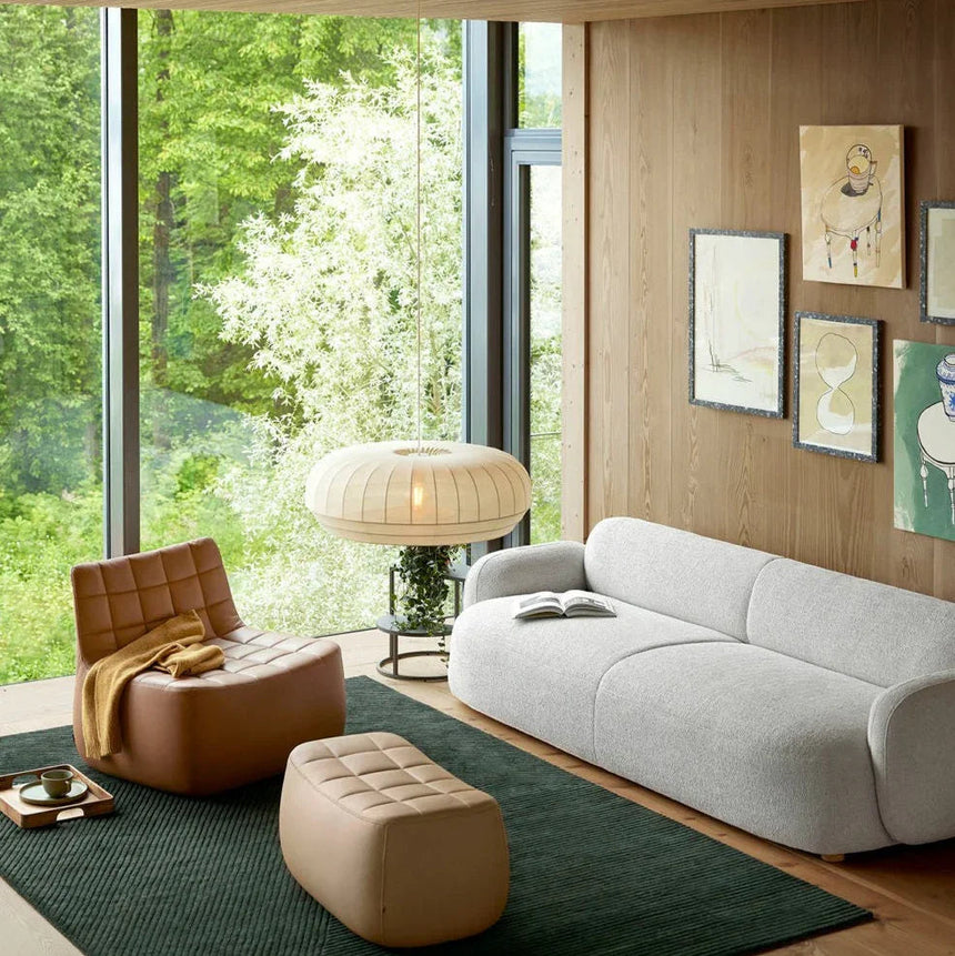 Broad knitted cloth shade lit above a sofa in front of a garden window