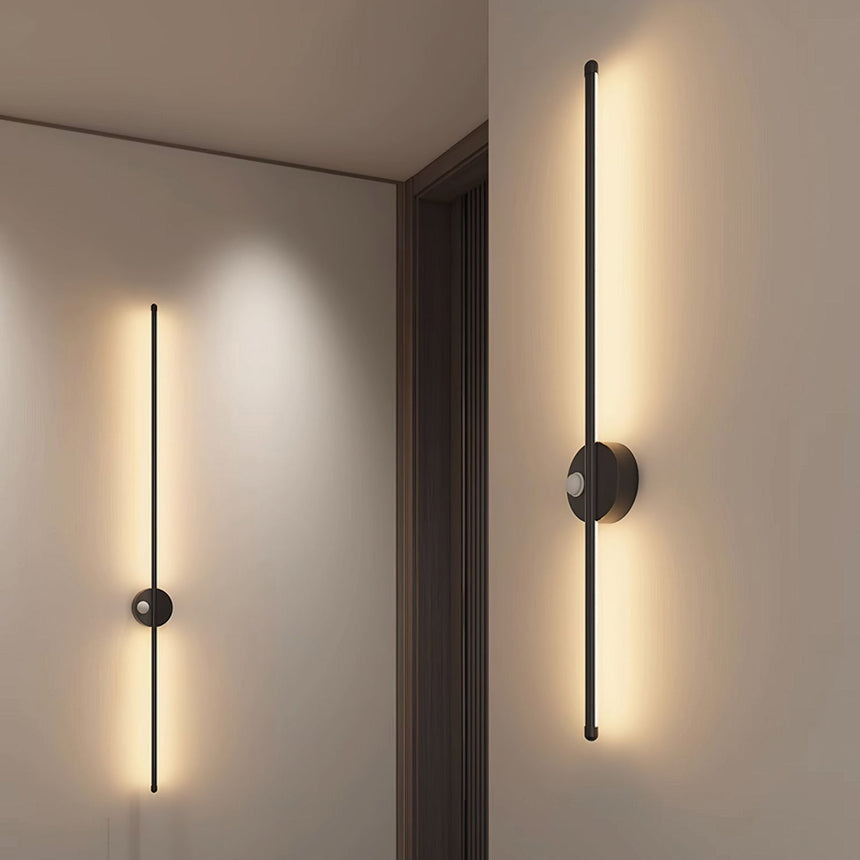 Two rods lit along a hallway wall beside a doorway and a run of pale doors