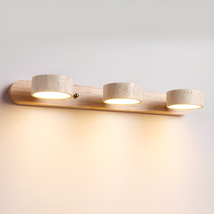 Three travertine discs lit on a light wood bar against a plain wall