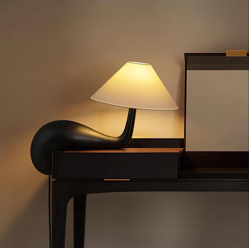 Dark wood desk lamp lit at the edge of a black desk beside a mirror