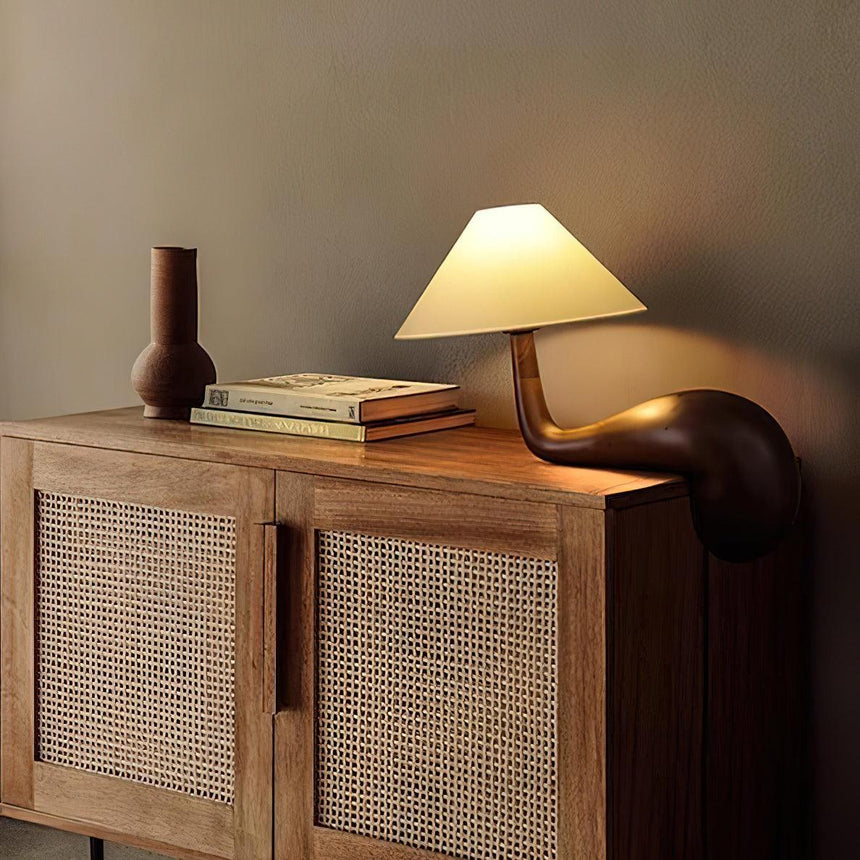 Wood desk lamp lit on a cane fronted cabinet beside a vase