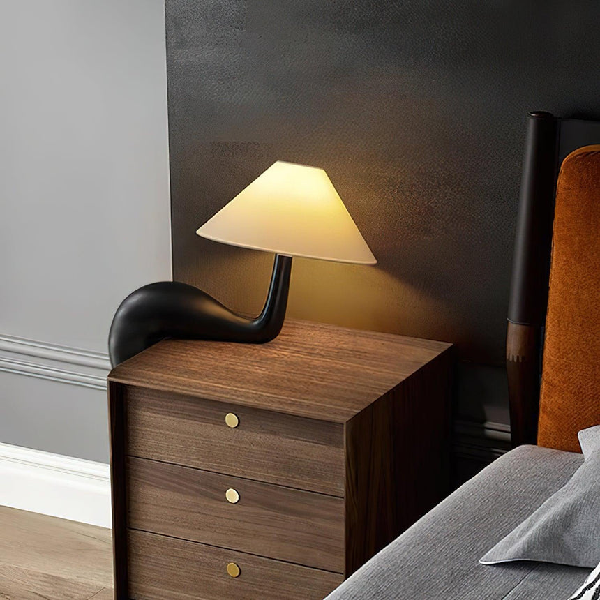 Black wood desk lamp lit on a chest of drawers in a dark room