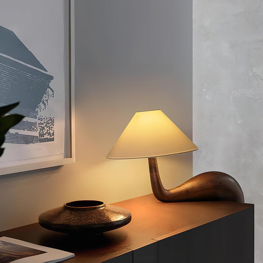 Wood desk lamp lit on a dark shelf beside a woven bowl