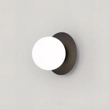 Frosted glass LED wall lamp in matte black finish mounted beside a bed in a modern Nordic bedroom