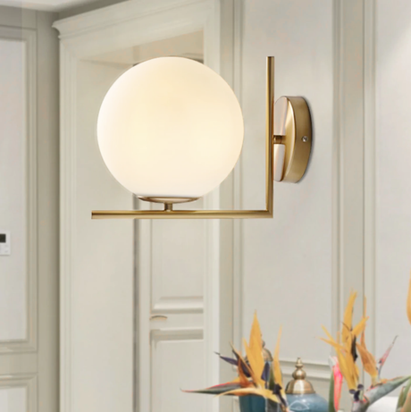 Brass wall sconce LED globe design mounted on a neutral living room wall with warm ambient glow