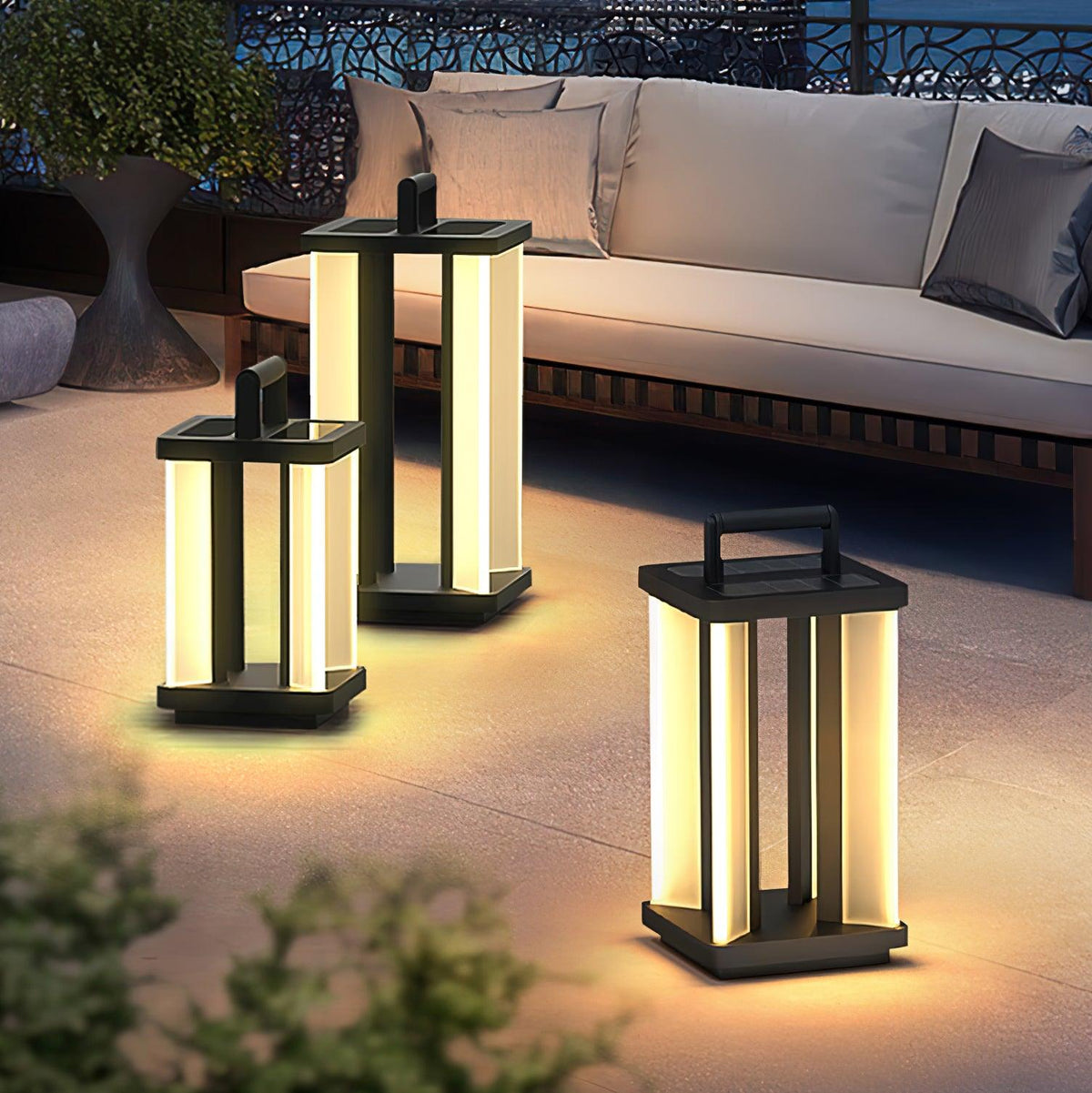 Three outdoor lantern lights grouped on a terrace floor beside a pale sofa