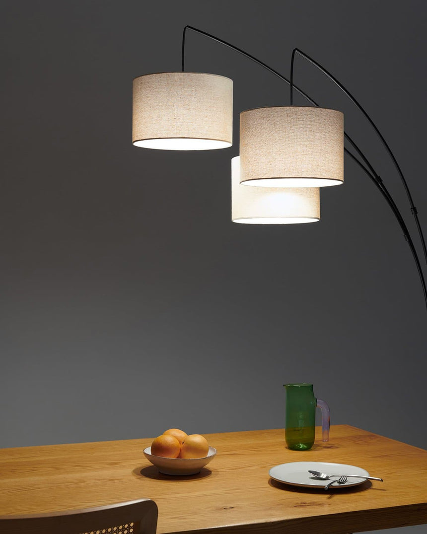 Black three arm lamp lit over a wood dining table against a dark wall
