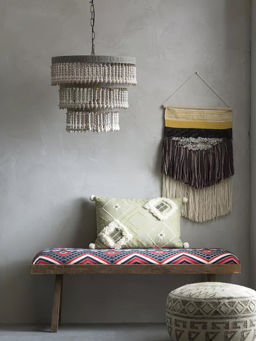 Lit above a patterned bench and a woven wall hanging against a gray wall