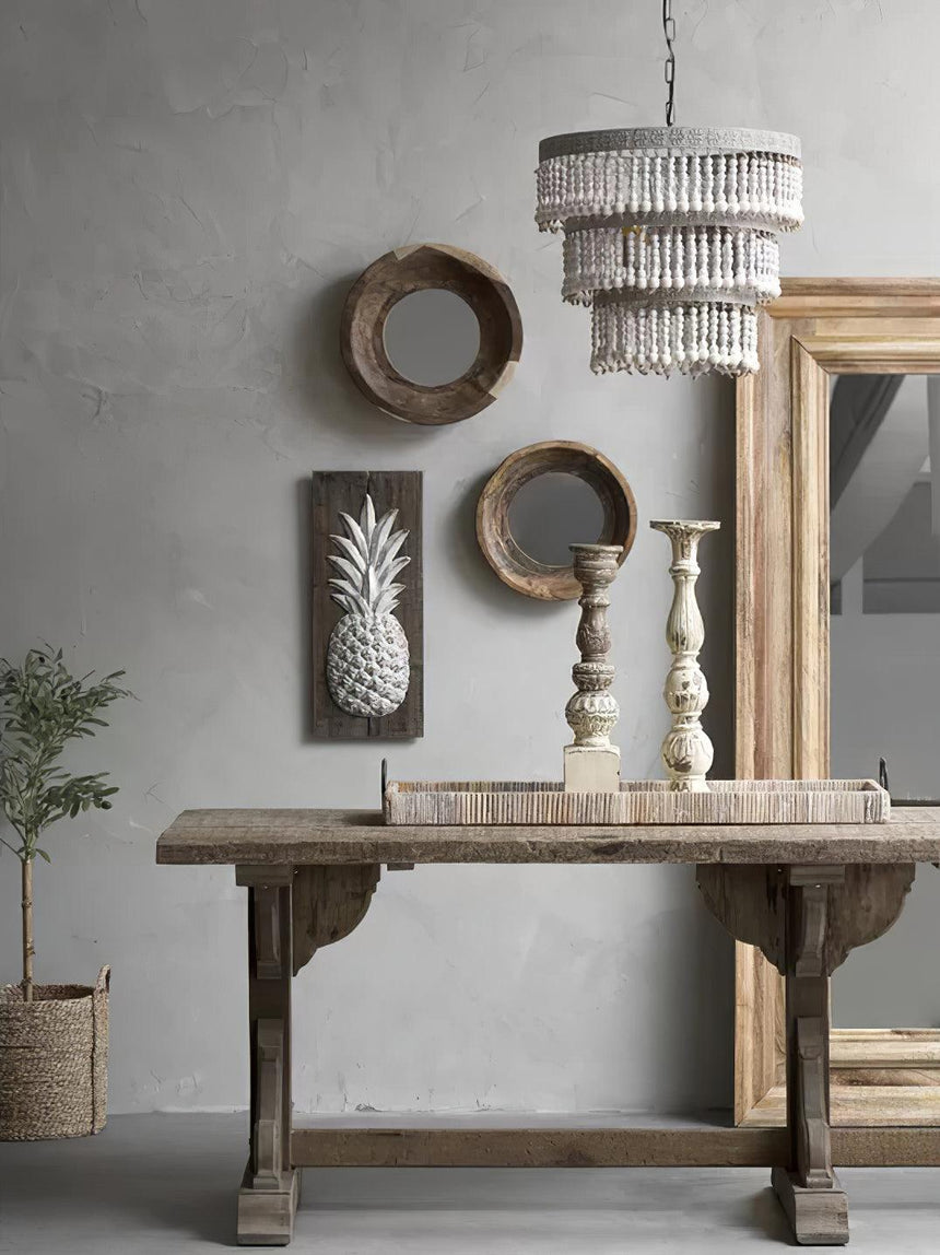 Hung above a weathered console table with round mirrors and candlesticks